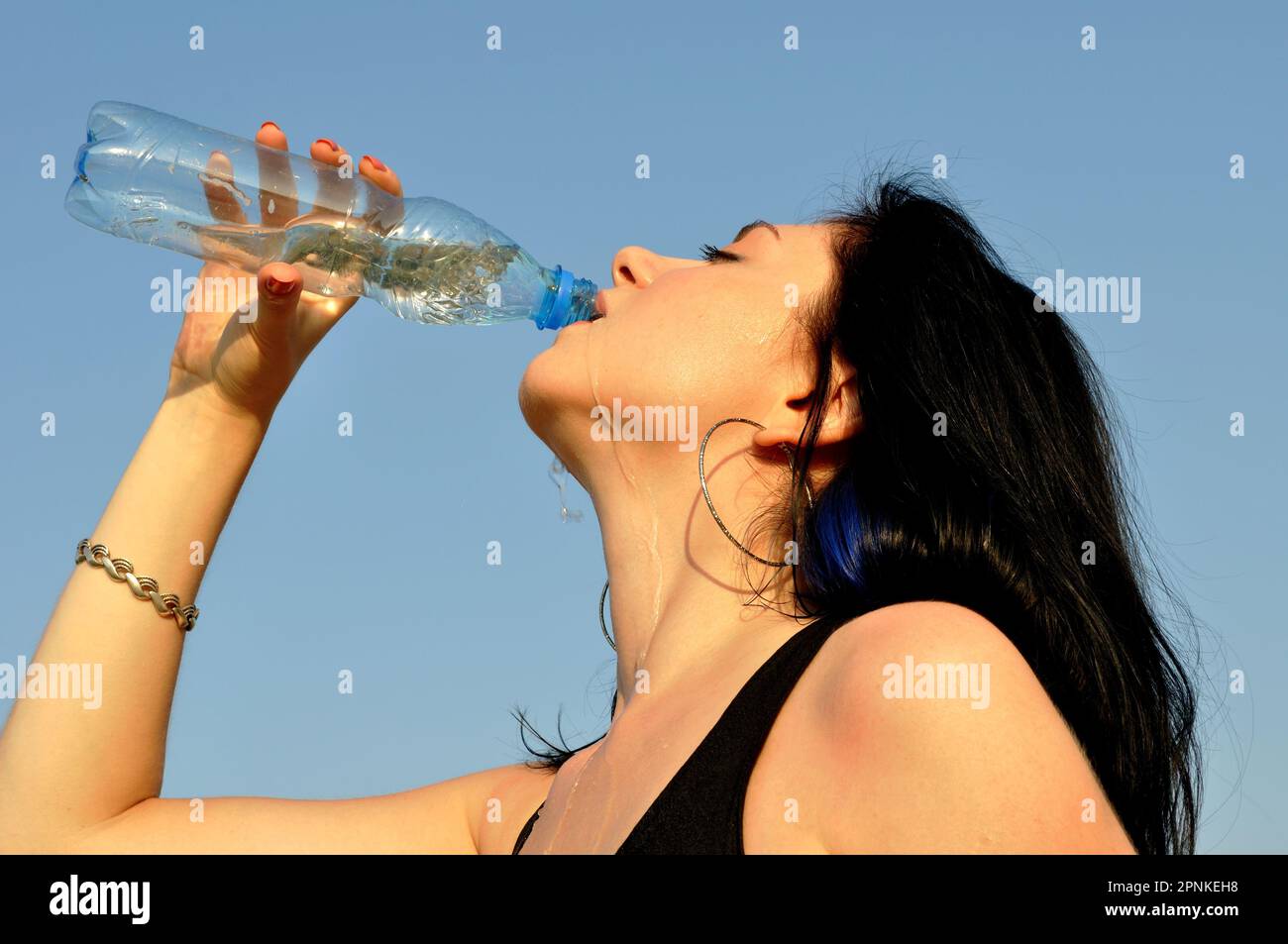 giovane donna attraente beve acqua fredda in giornata calda su sfondo cielo blu Foto Stock