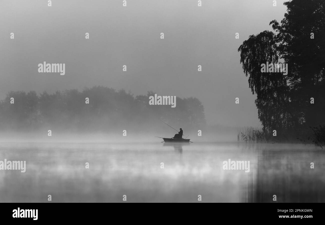 Una barca pescatore su un lago in una mattina nebbia Foto Stock