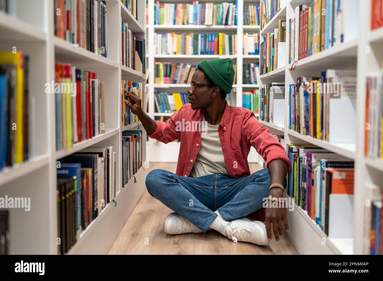 Studente penoso uomo afroamericano scelta di libri di testo di ricerca in biblioteca universitaria. Foto Stock