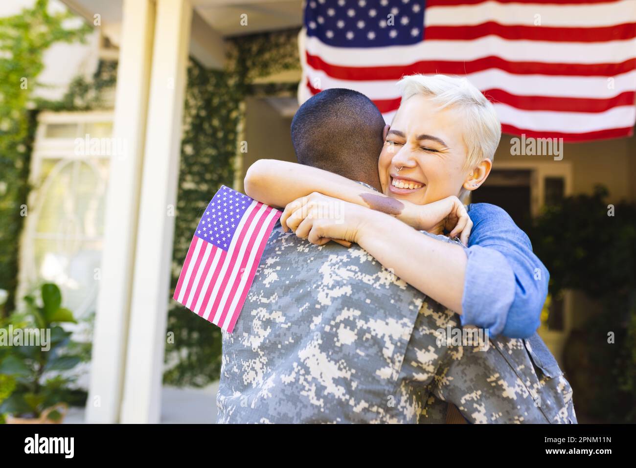 Donna caucasica felice e soldato americano maschio biraciale che abbraccia fuori casa Foto Stock