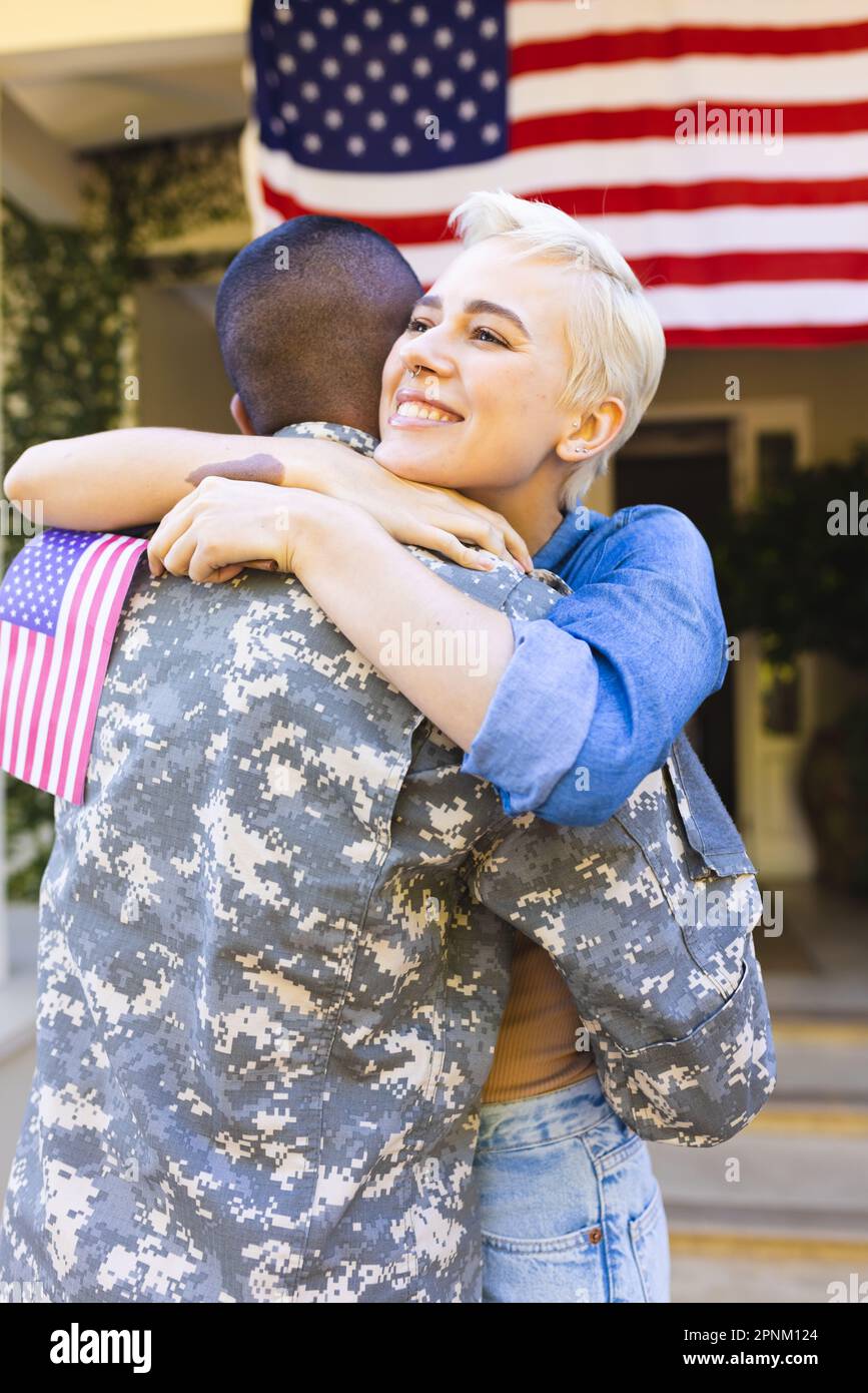 Donna caucasica felice e soldato americano maschio biraciale che abbraccia fuori casa Foto Stock