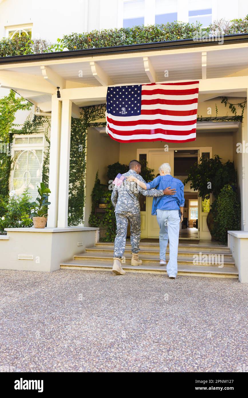 Donna caucasica felice e soldato americano maschio biraciale che abbraccia fuori casa Foto Stock