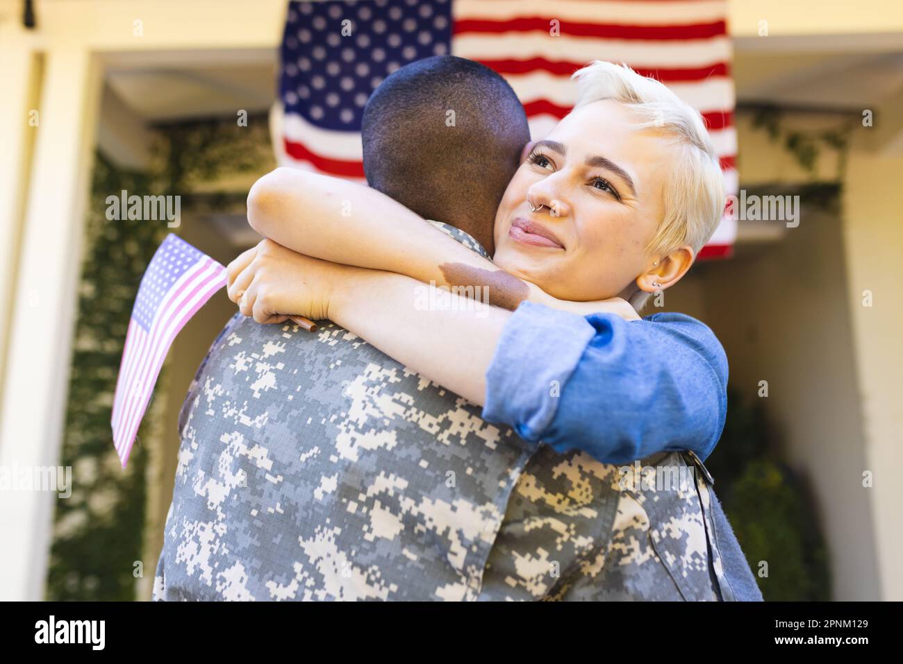 Donna caucasica felice e soldato americano maschio biraciale che abbraccia fuori casa Foto Stock