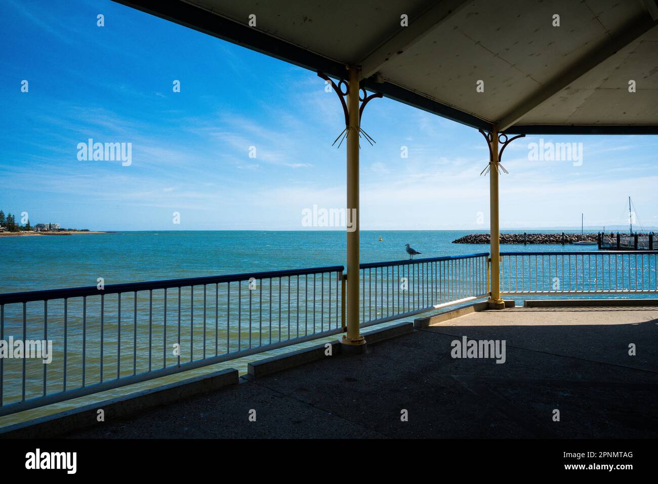 Vista sull'oceano dall'interno del molo con gabbiano appollaiato sulla ferrovia Foto Stock