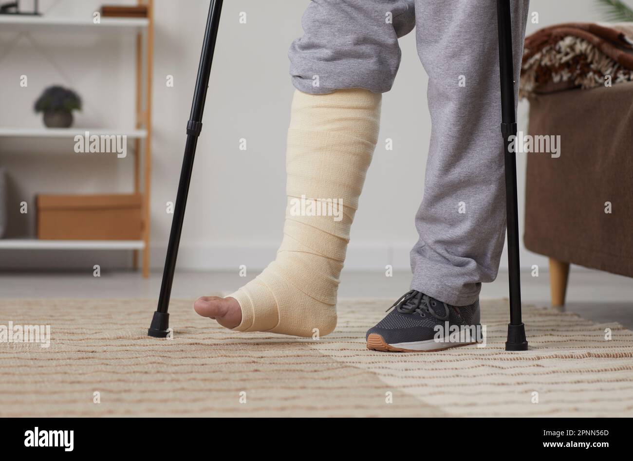 Un giovane uomo malsano con lesioni alle gambe o ai piedi rotte è in fase di riabilitazione a casa. Foto Stock