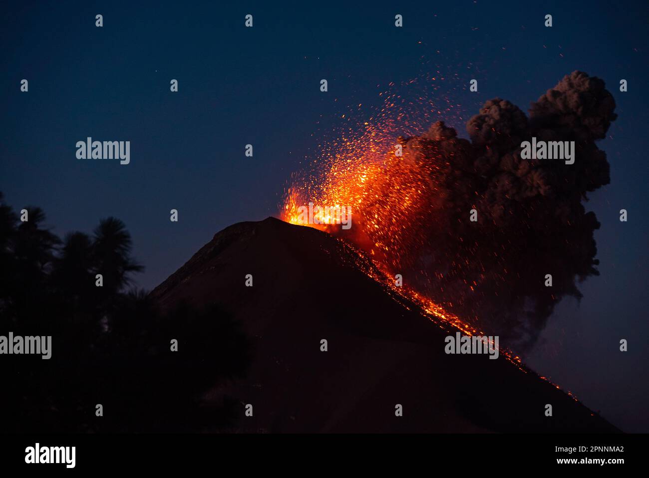 Uno spettacolare scatto notturno di un vulcano con una cascata di lava incandescente lungo il suo lato Foto Stock