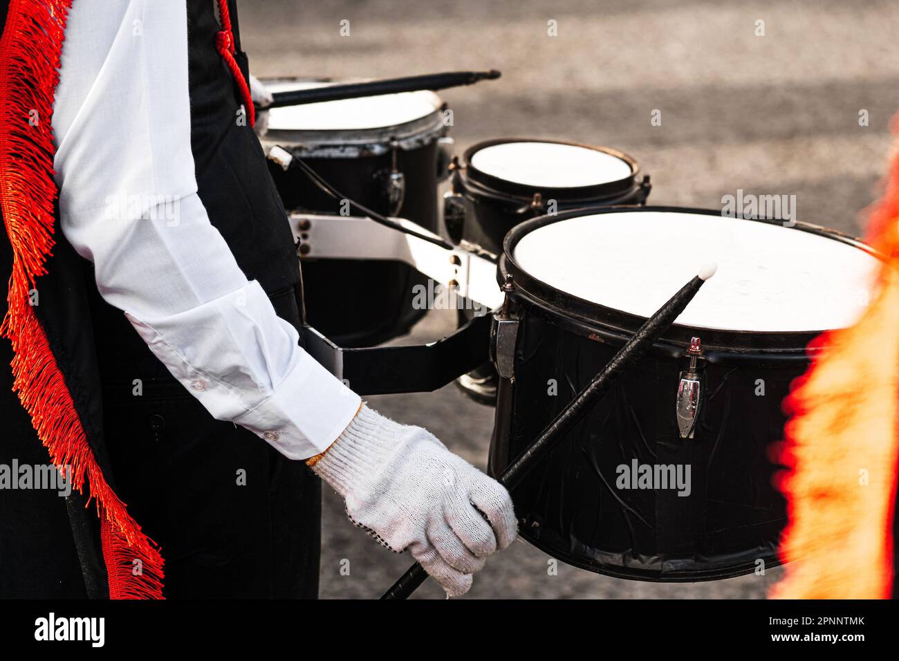 Mani di una persona che tiene i bastoni di batteria che gioca in una banda marching. Foto Stock