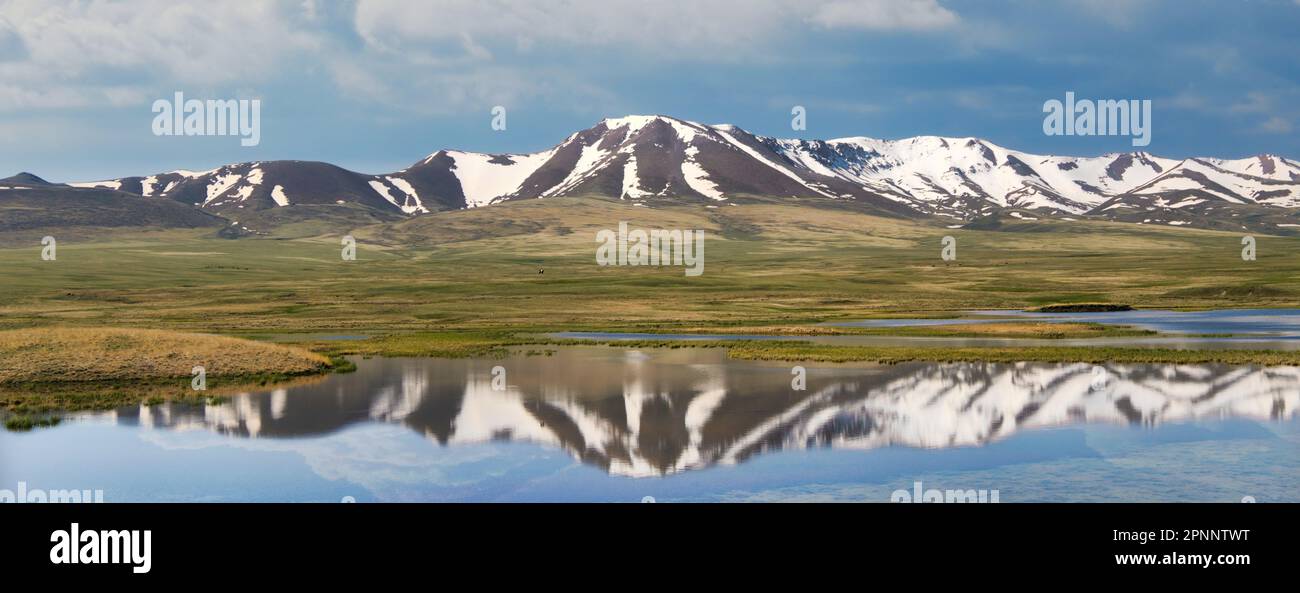 Kirghizistan natura verde paesaggio con un lago riflesso e vaste montagne. Il Kirghizistan è un paese senza sbocco sul mare situato nell'Asia centrale, noto per la sua Foto Stock