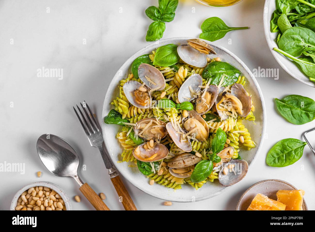 Pasta fusilli alle vongole Pasta di pesce con vongole, parmigiano, spinaci e pinoli con posate su fondo bianco. Vista dall'alto Foto Stock