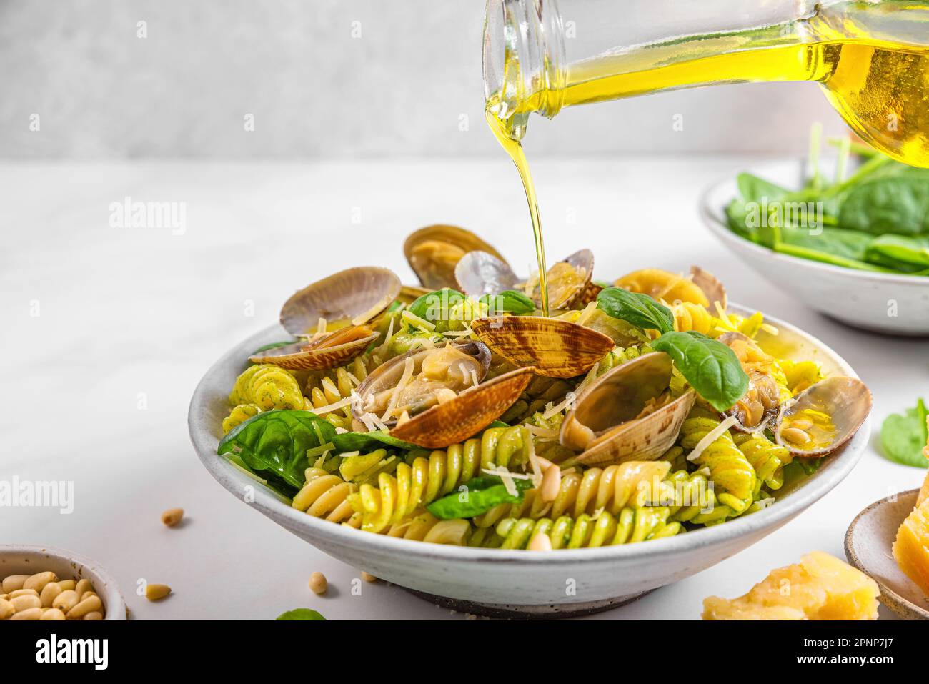 Versare l'olio d'oliva in pasta di pesce con vongole di vongole di vongole, parmigiano, spinaci, pinoli. Cucina italiana. Dieta mediterranea Foto Stock