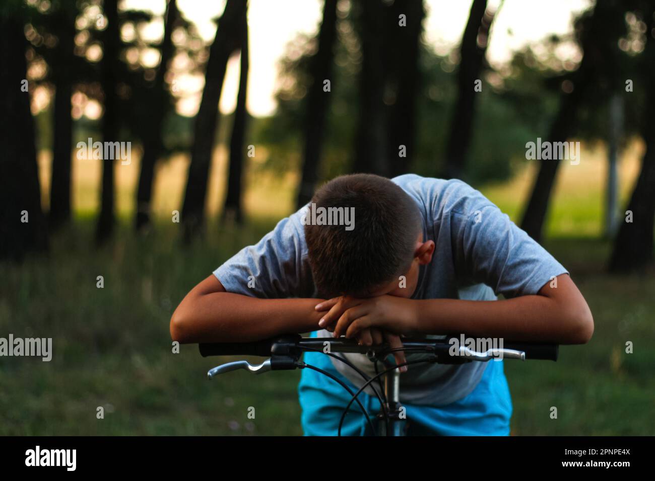 Triste ragazzino seduto in bicicletta vicino alla foresta. Bambino piangere e nascondere il suo volto. Bambino da solo. Vittima di un rigonfiamento. Problema a scuola. Protezione sociale. Teen Foto Stock