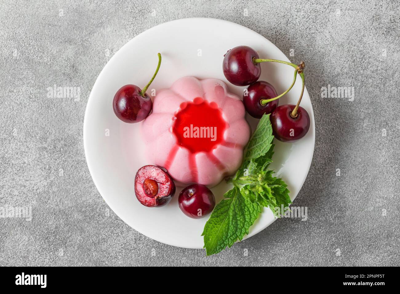 Dessert di panna cotta alla ciliegia italiana con frutti di bosco freschi, sciroppo e foglia di menta su sfondo grigio. Vista dall'alto. Cibo gustoso. Foto Stock