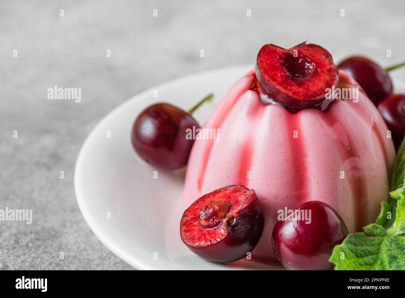 Dessert di panna cotta alla ciliegia italiana con frutti di bosco freschi, sciroppo e foglia di menta su sfondo grigio. Primo piano. Cibo gustoso. Foto Stock