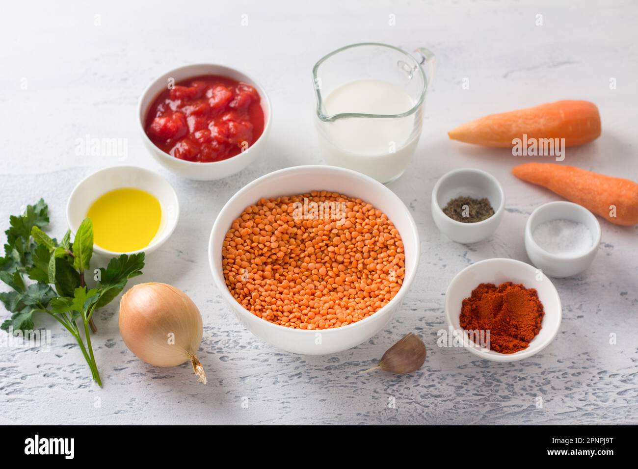 Ingredienti per la zuppa cremosa di lenticchie: Lenticchie rosse, cipolla, carota, aglio, passata di pomodoro, panna, olio d'oliva, paprika affumicata, sale, pepe, erbe su un lig Foto Stock