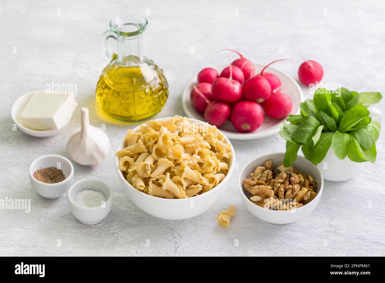 Ingredienti per insalata, pasta e altri piatti vegetariani: Pasta, ravanello, rucola, noci, feta, aglio, olio d'oliva, sale e pepe macinato su un g Foto Stock
