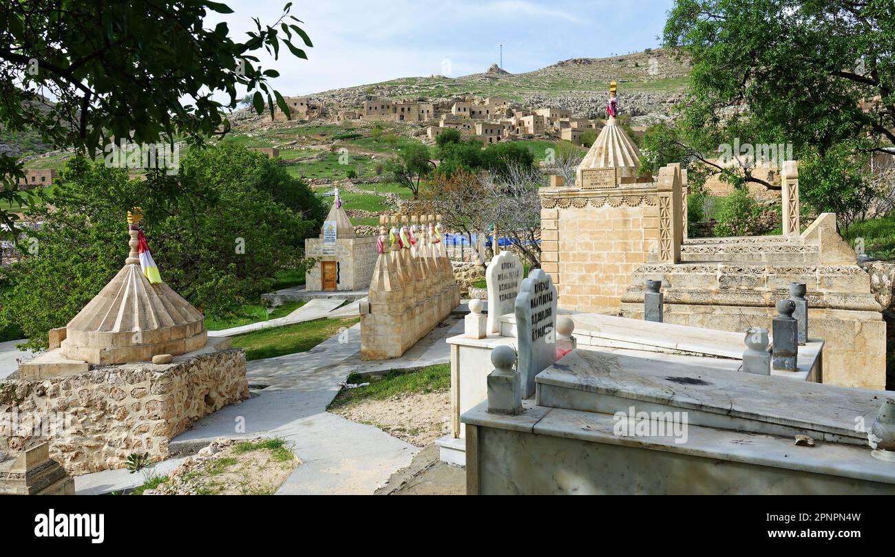 Il cimitero di Yazidi nel villaggio di Kiwêxê nel distretto di Midyat. Sullo sfondo, si possono vedere le case del villaggio che sono state completamente vuote per molti anni e alcune di loro sono state distrutte. I curdi Yazidi che vivono nel villaggio di Bacine del distretto di Midyat e i distretti di Besiri in Turchia hanno celebrato la festa del mercoledì rosso, conosciuta come 'Charshema Sor' in curdo, con gioia con vari intrattenimenti. Uomini, donne e bambini di 10 famiglie Yazidi che vivono nel villaggio di Bacine si sono riuniti al Centro Culturale Yazidi dopo le preghiere del mattino, indossando gli abiti più colorati e belli. Yazidis credere t Foto Stock