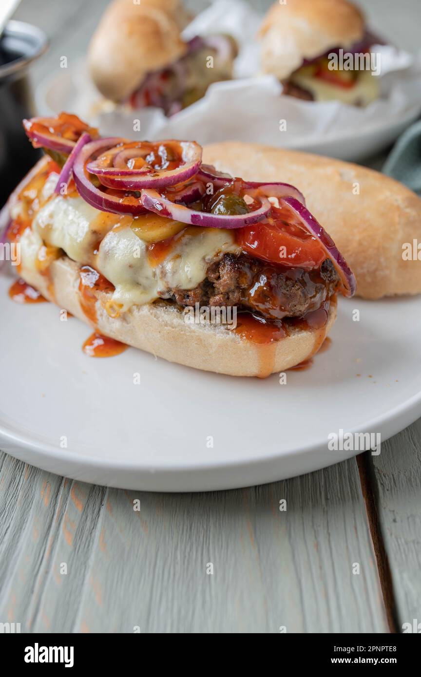 Cheeseburger su baguette francese con pomodori, sottaceti, cipolle rosse e salsa barbecue fatta in casa. Foto Stock