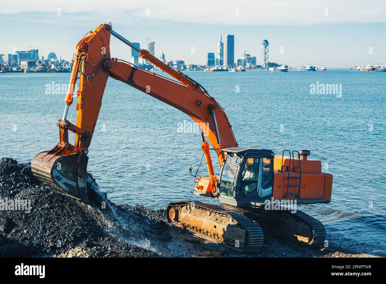 Scavatore o scavatore che lavora sulla movimentazione del terreno presso lavori di protezione della riva a Batumi. Il retroescavatore arancione scava sabbia e ghiaia in cava. Digger durante lo scavo Foto Stock