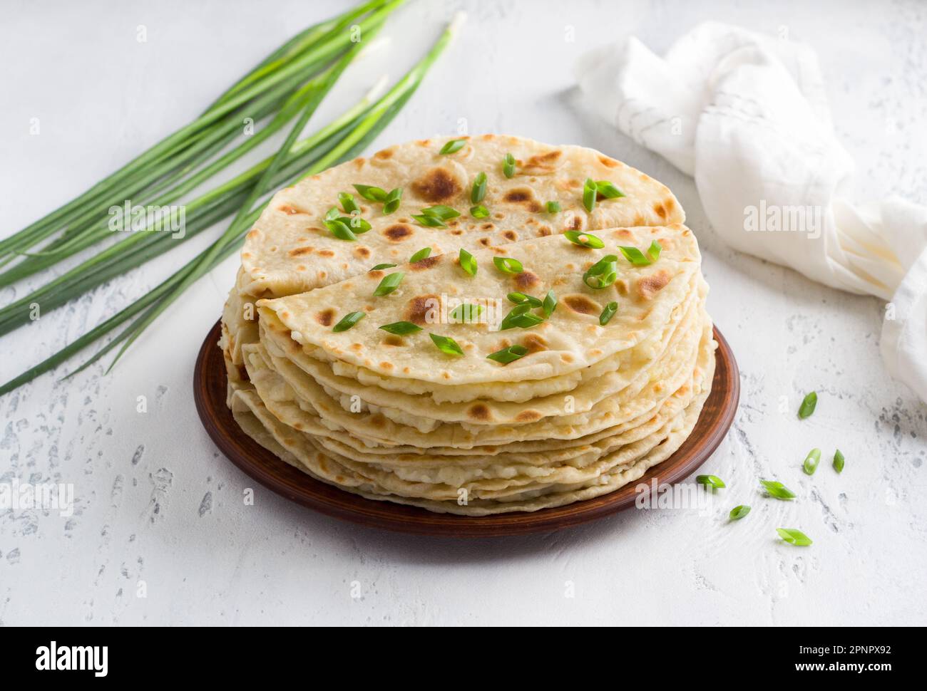 Tradizionale pane piatto tataro, kastyby e un mazzo di cipolle verdi su uno sfondo grigio chiaro Foto Stock