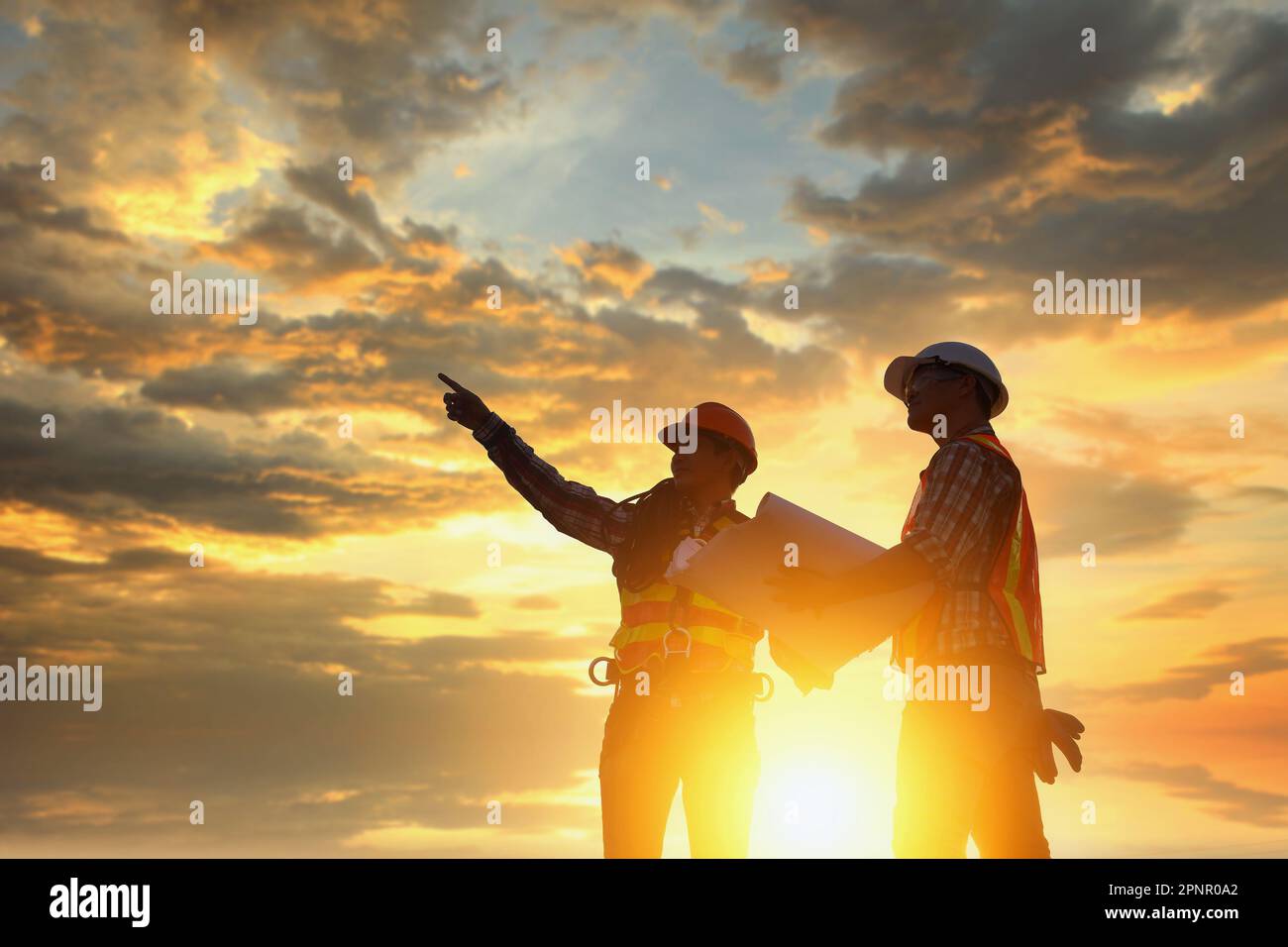 Silhouette di due ingegneri di costruzione in piedi su un cantiere di supervisione di un progetto di costruzione al tramonto, Thailandia Foto Stock