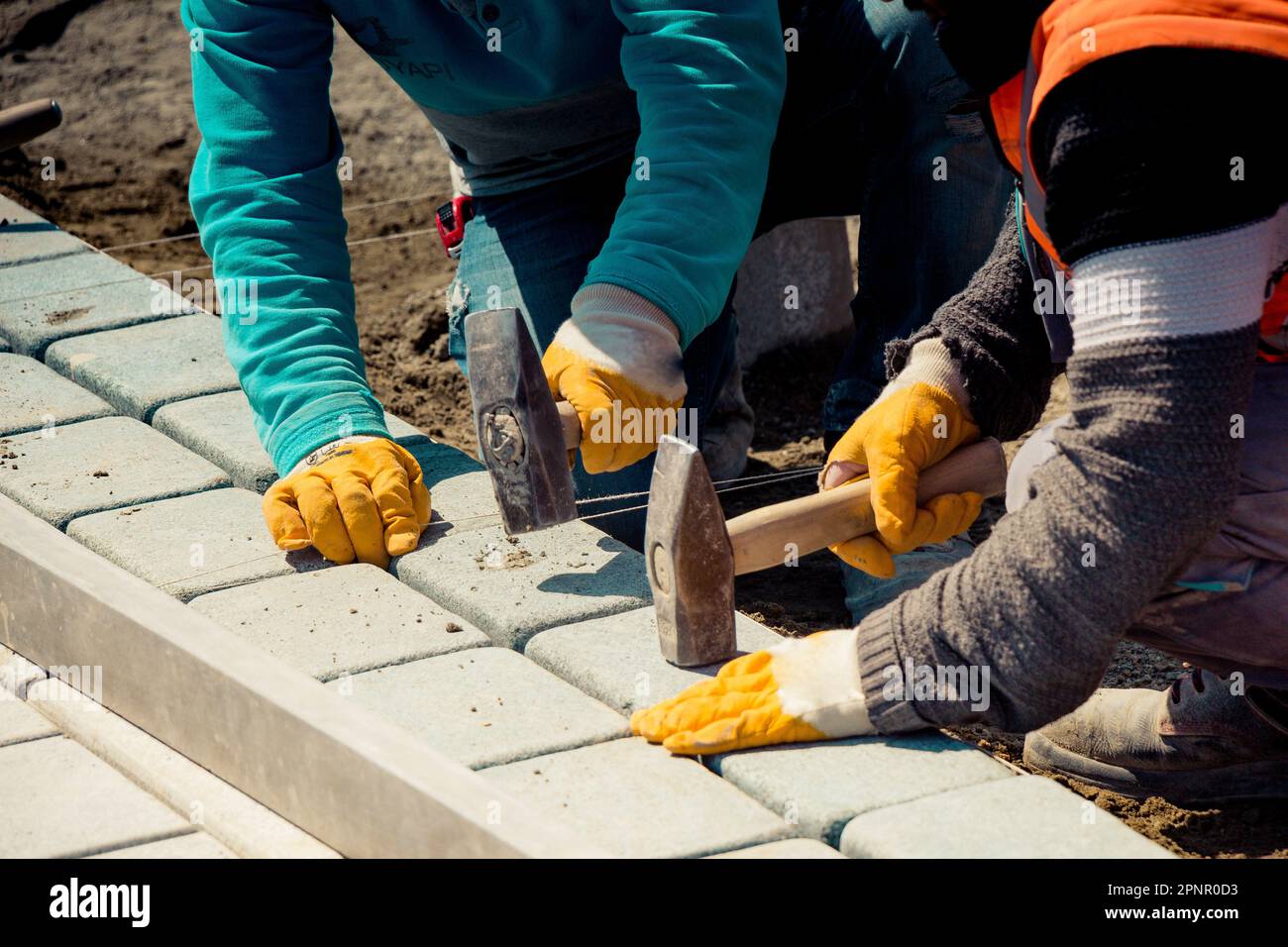Primo piano di due costruttori che posano pietre da pavimentazione in granito Foto Stock
