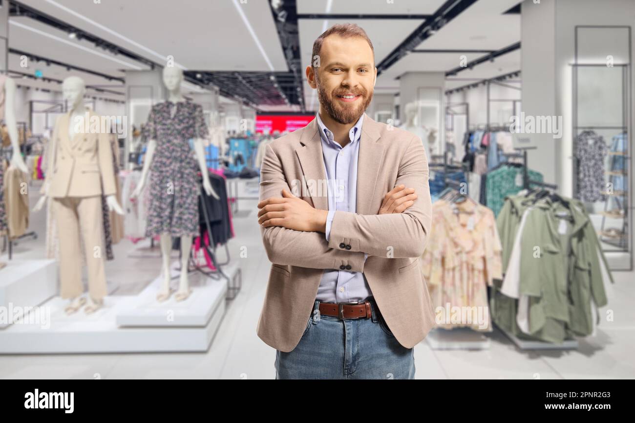 Uomo professionista in tuta beige e jeans in posa con le braccia incrociate in un negozio di abbigliamento Foto Stock