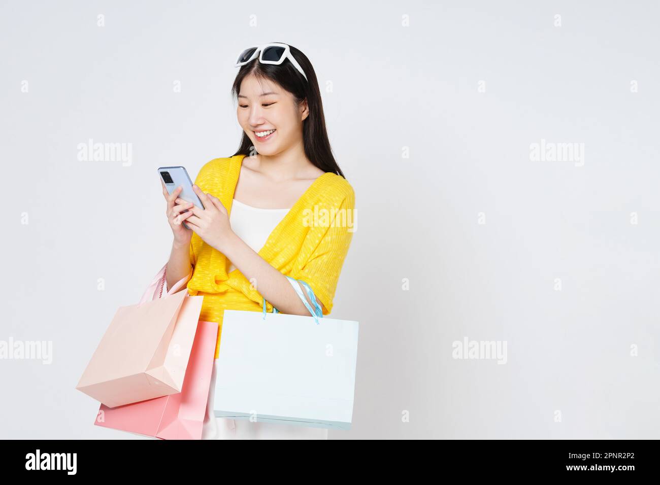 Giovane donna che tiene le borse della spesa mentre si utilizza il telefono cellulare isolato su sfondo bianco. Foto Stock
