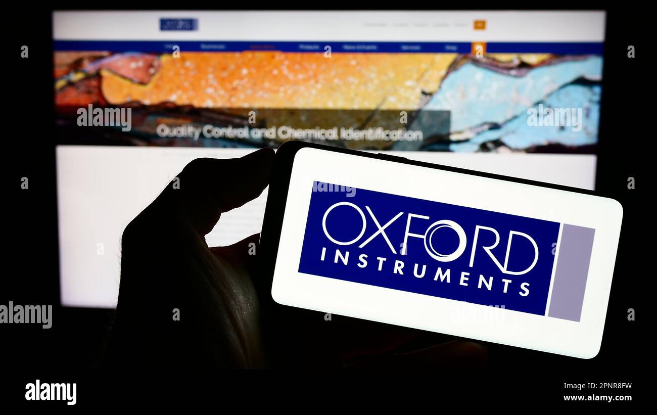 Persona che tiene il cellulare con il logo della società britannica Oxford Instruments plc sullo schermo di fronte al sito web aziendale. Messa a fuoco sul display del telefono. Foto Stock
