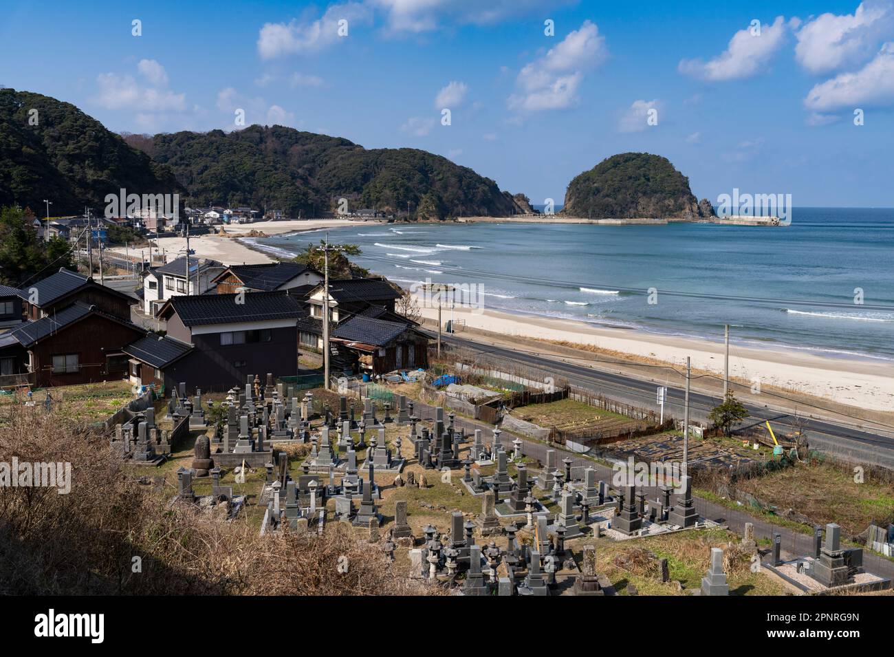 Una piccola città che include un cimitero e una spiaggia sul Mare del Giappone visto da un treno sulla linea Sanin vicino a Iwami nella prefettura di Tottori, Giappone. Foto Stock