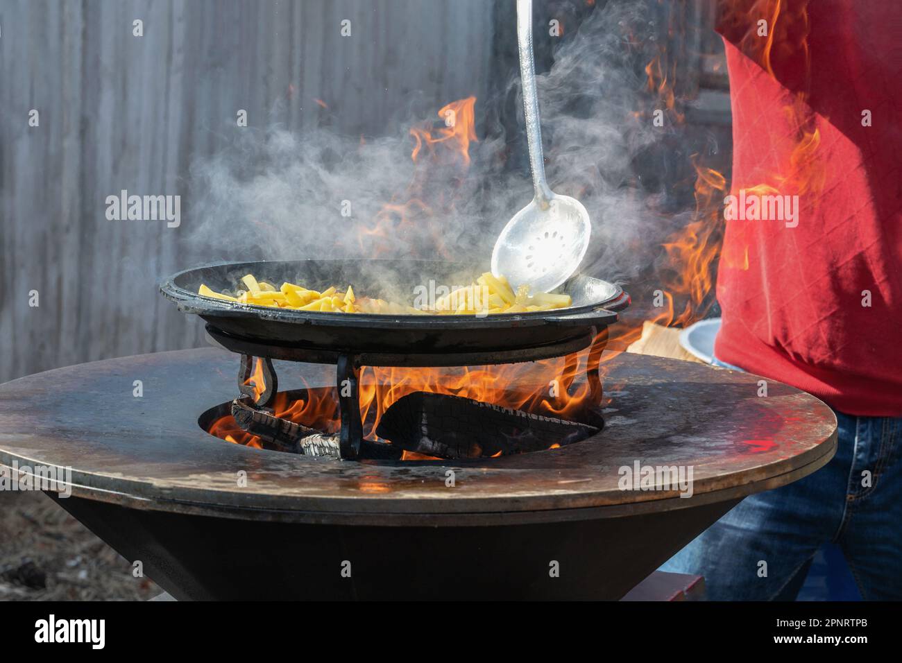 Le verdure sono tostate su un focolare rotondo. Griglia rotonda a forma di ciotola con un fuoco all'interno. L'uomo prepara il focolare per il barbecue. La legna da ardere sta bruciando Foto Stock