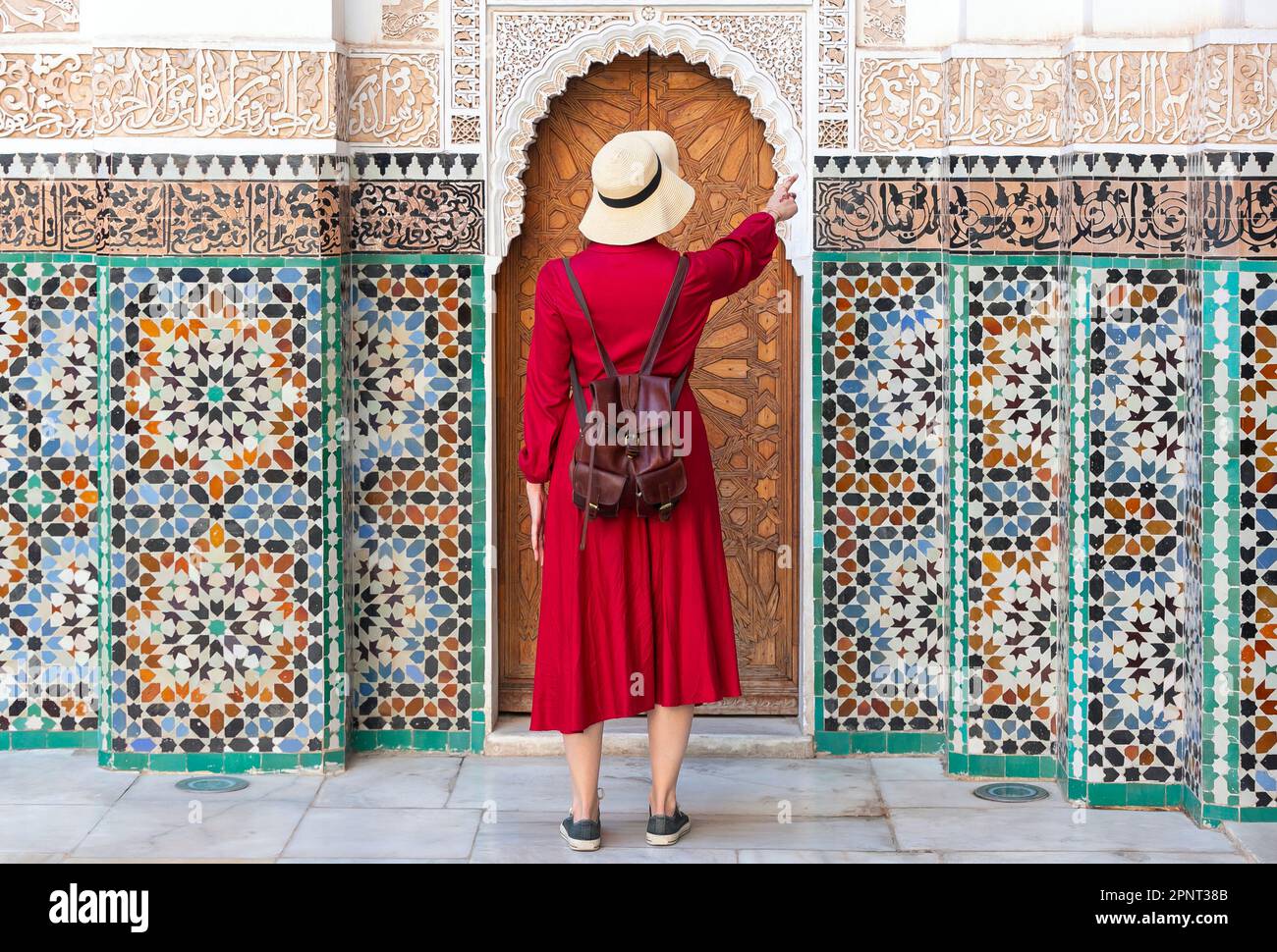 Ragazza vestita in rosso con cappello guardando il ben Youssef Madrasa a marrakech, marocco Foto Stock