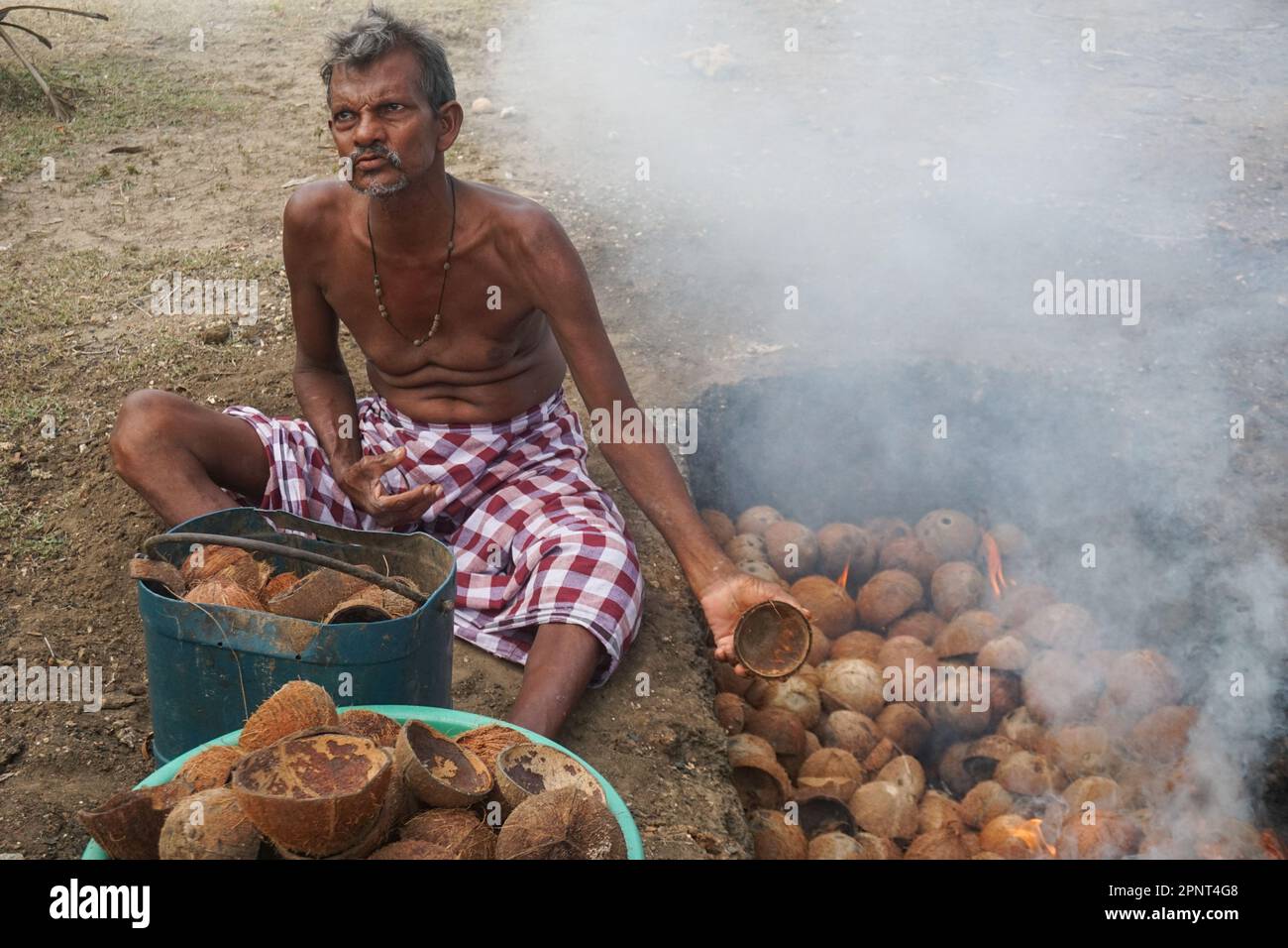 John Mary Visuvasam brucia le conchiglie di cocco in una fossa a Kayts, distretto di Jaffna, Sri Lanka il 3 settembre 2021. Le noci di cocco sono usate per cucinare, ma le conchiglie sono in genere scartate, così Visuvasam raccoglie e le brucia per fare carbone da vendere. (Pashna Alistan/Global Press Journal) Foto Stock