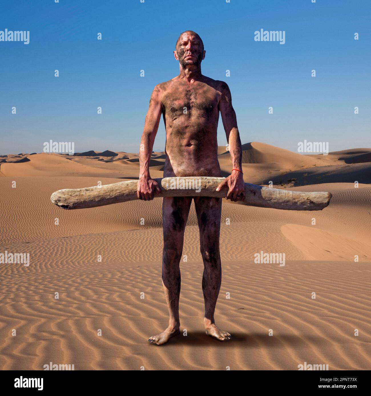 Nudo uomo coperto di sporcizia che tiene driftwood sulla duna di sabbia Foto Stock