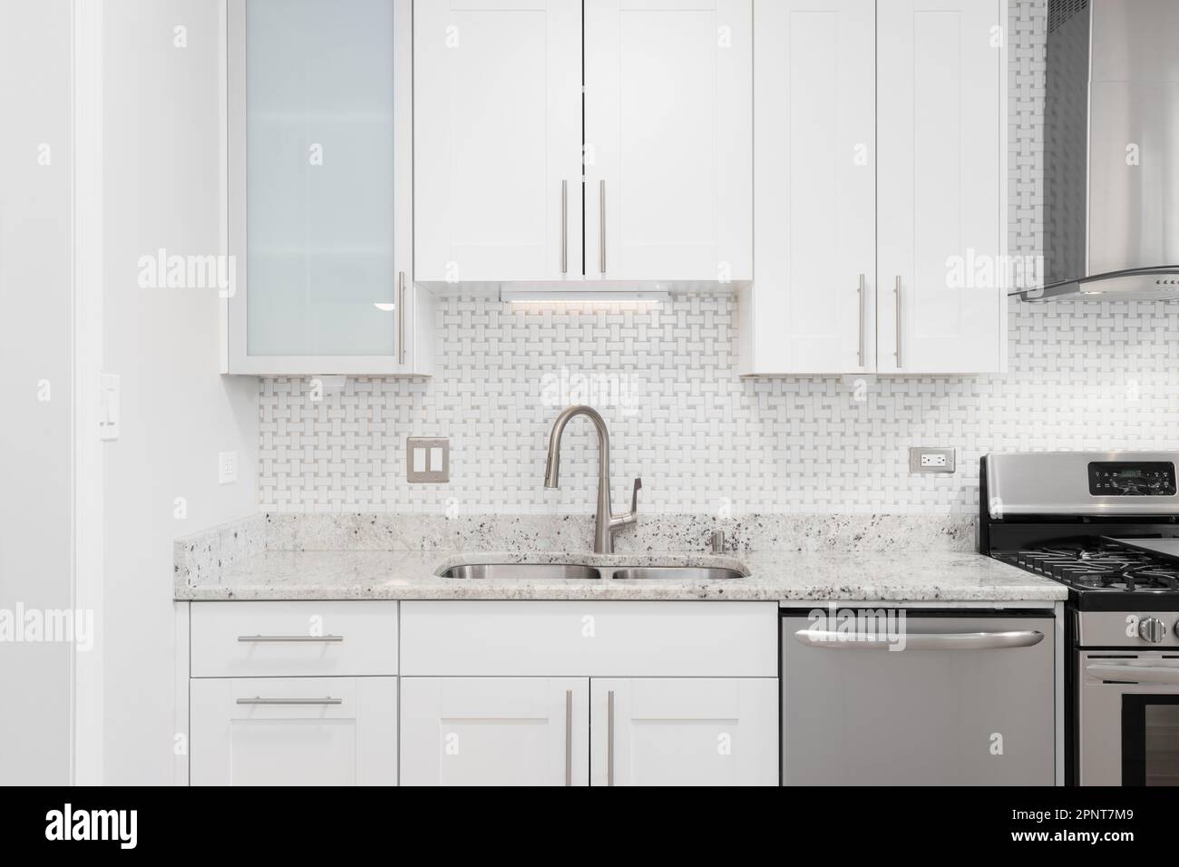 Una bella cucina bianca dettaglio girato con un backsplash piastrellato, armadi bianchi, elettrodomestici in acciaio inossidabile, e banco in marmo. Foto Stock