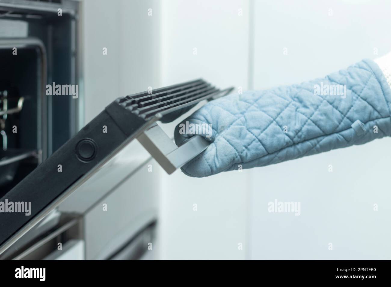 Cucina casalinga: La mano protetta da guanto da cucina apre la porta del forno Foto Stock