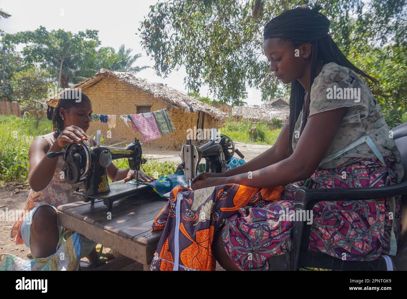 Maguy Yohali, a sinistra, e Sarha Kiyasula cucì vestiti all'aperto nel loro quartiere a Kisangani, Repubblica Democratica del Congo il 17 maggio 2022. (Ehlen Mbuyi Mutombo/Global Press Journal) Foto Stock