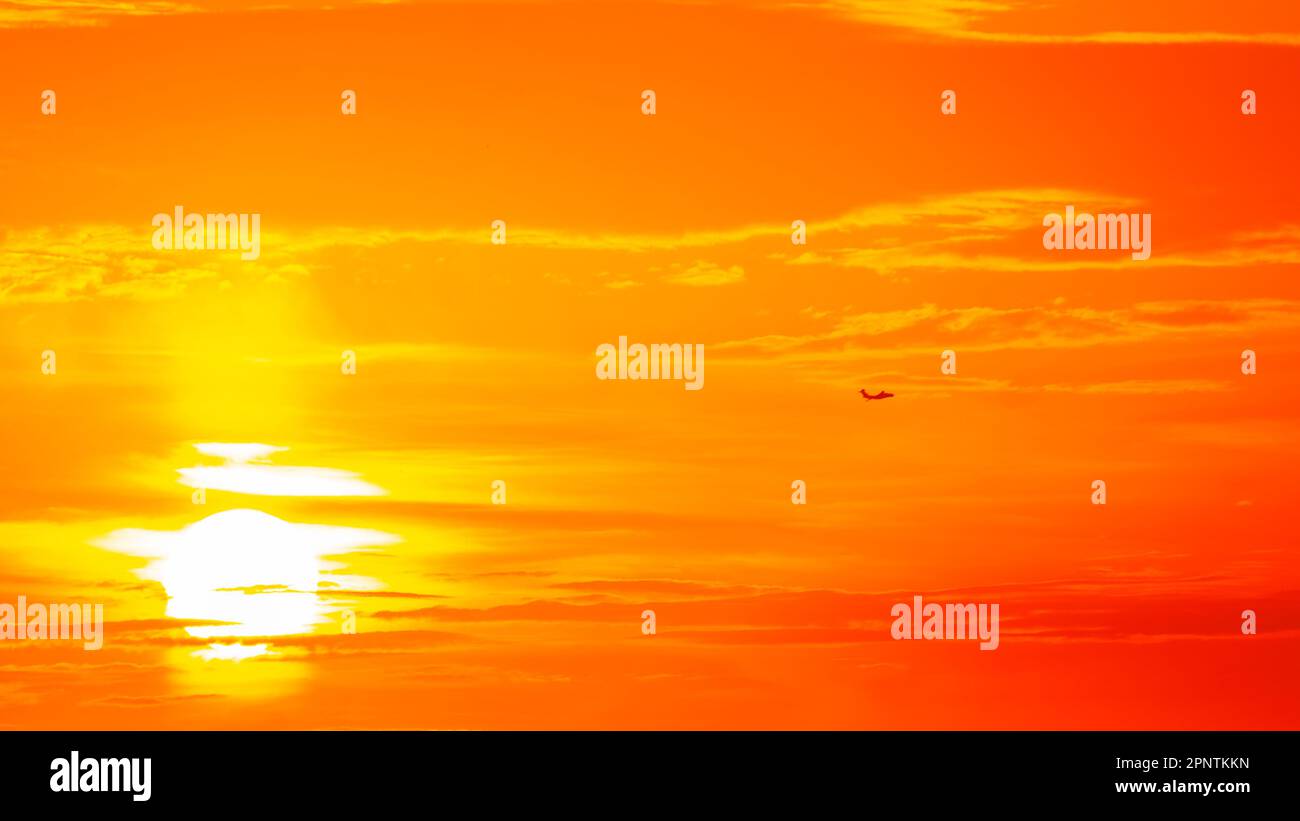 Un cielo arancione brillante, la silhouette di un aereo volante e un sole luminoso Foto Stock