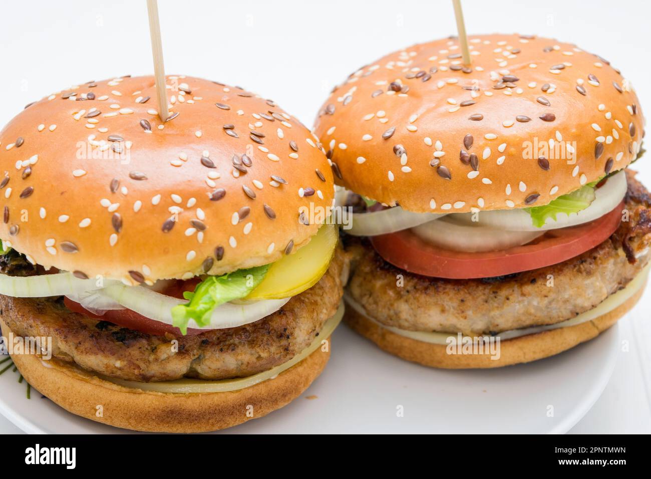 Una splendida vista di un grande hamburger con pomodori, cipolla, cetriolo su un piatto bianco Foto Stock