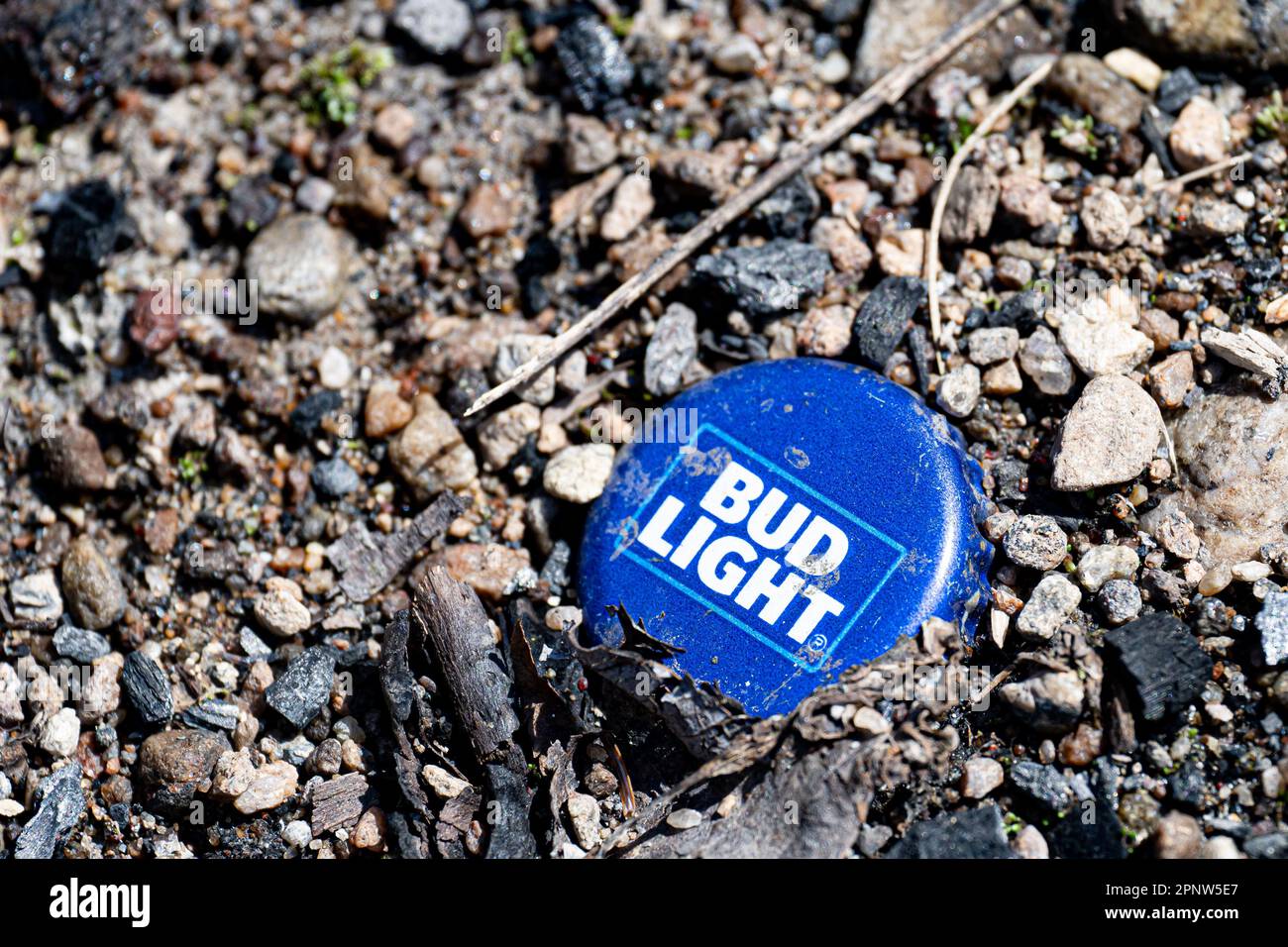 Un tappo della bottiglia di birra Bud Light blu e bianco sporco scartato e schiacciato nello sporco in un fossa di fuoco nelle montagne Adirondack, NY USA Foto Stock