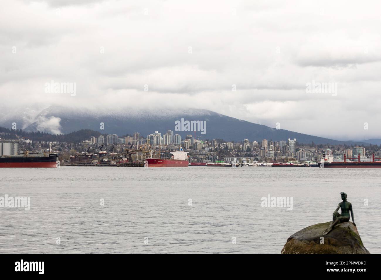 Un North Vancouver piovoso è visto da Stanley Park a Vancouve, Canada. In primo piano c'è la famosa statua "Girl in a wetsuit" di Elek Imredy. Foto Stock