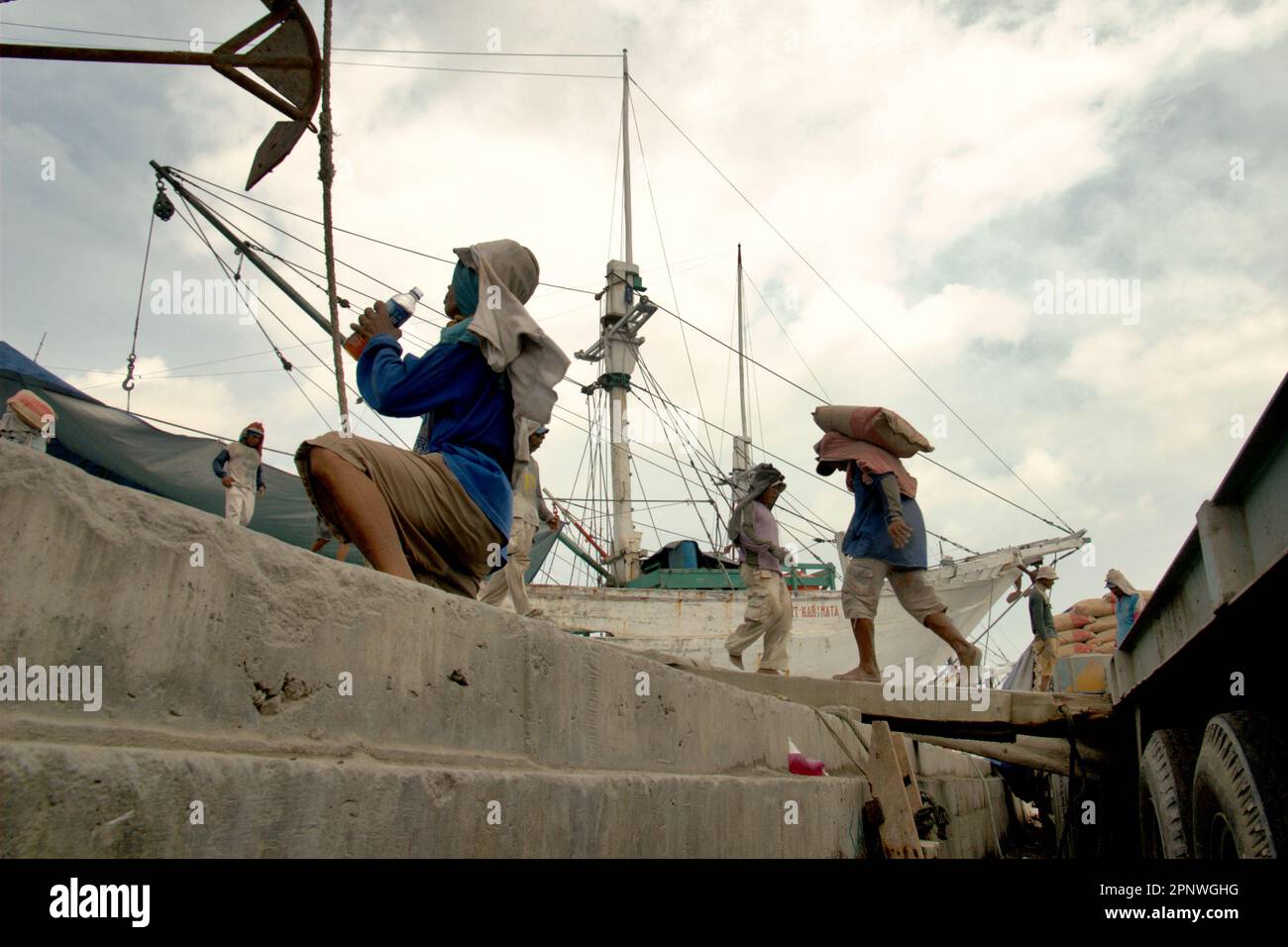 Un lavoratore beve acqua da una bottiglia di plastica mentre sta prendendo una pausa dal trasporto di sacchi di cemento da un camion su una nave phinisi al porto tradizionale Sunda Kelapa a Penjaringan, a nord di Giacarta, Jakarta, Indonesia. Il cambiamento climatico esporrà sempre più i lavoratori esterni allo stress termico e alla riduzione della capacità di lavoro, secondo la relazione del 2023 pubblicata dal Gruppo intergovernativo sui cambiamenti climatici (IPCC), intitolata "cambiamenti climatici 2022: Impatti, adattamento e vulnerabilità”. Foto Stock