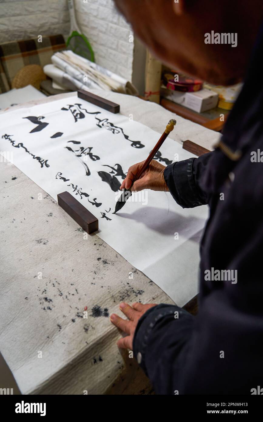Un vecchio calligrafo cinese sta scrivendo caratteri pennello, creando opere di calligrafia cinese. Traduzione: Viene la primavera, arriva il dio del vento. Foto Stock