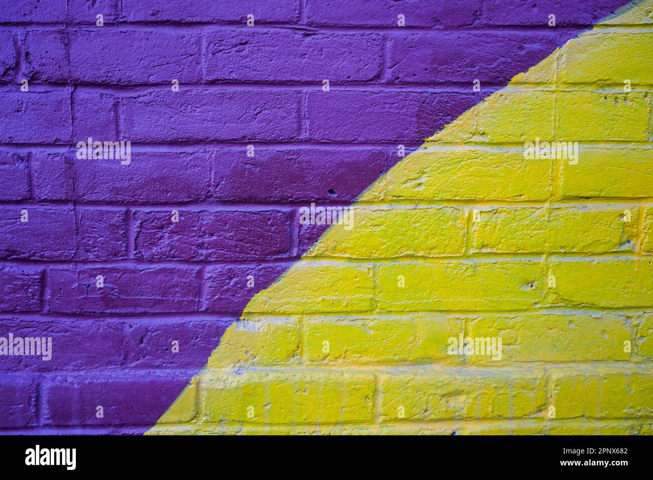 muro in mattoni con vernice spray viola e giallo Foto Stock