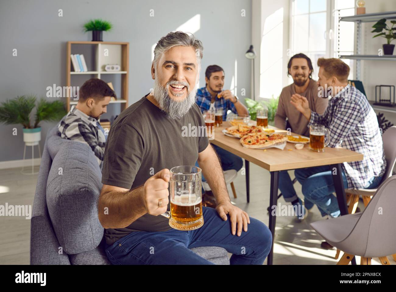 Ritratto dell'uomo bearded che tiene un bicchiere di birra con una compagnia di amici che parlano sullo sfondo. Foto Stock