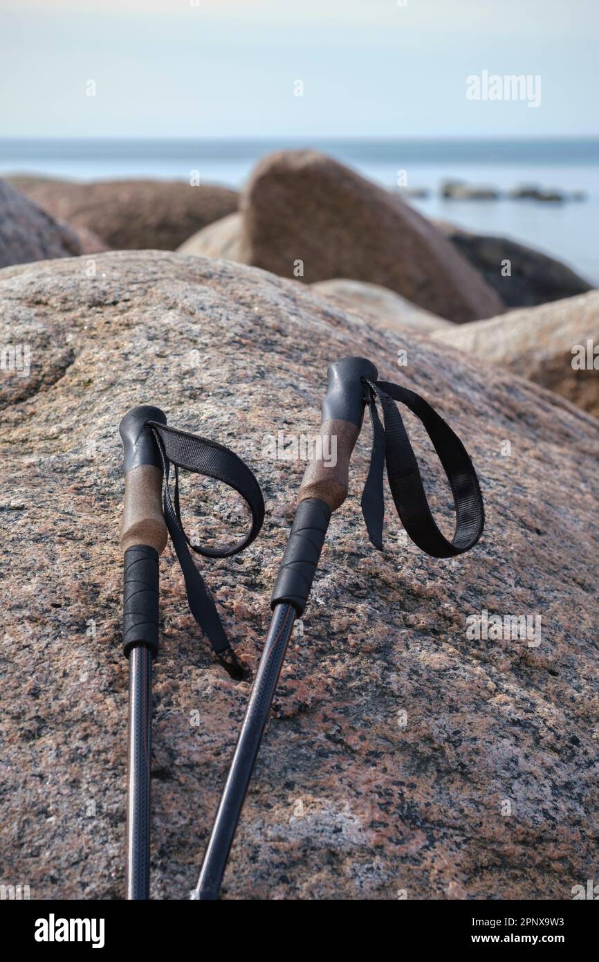 Bastoni da trekking punteggiati contro una grande roccia sulla riva del mare Foto Stock
