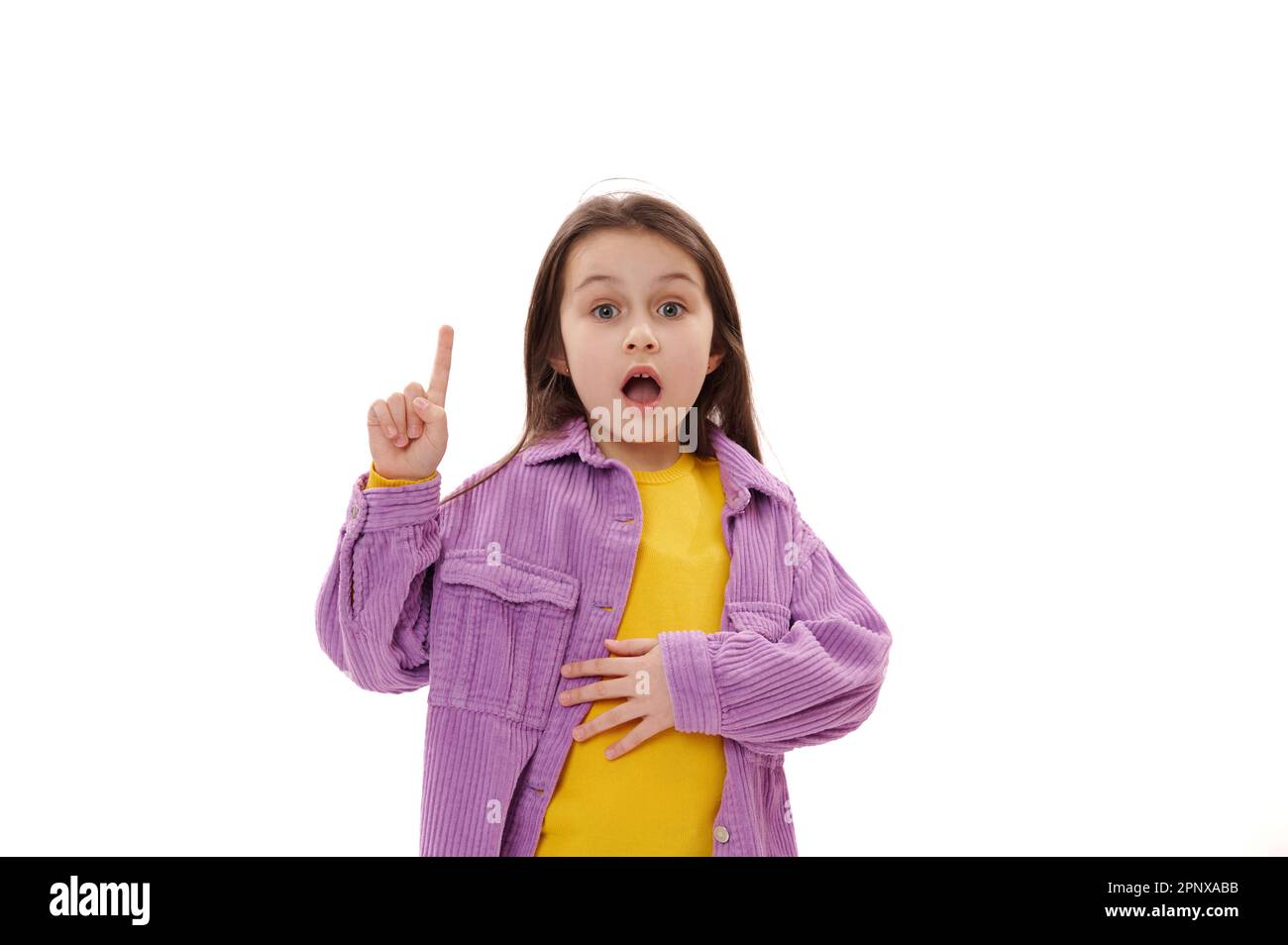 Ragazza bambino eccitato stupito che punta il dito indice da parte in su, guardando la macchina fotografica con la sua bocca aperta, sfondo bianco Foto Stock