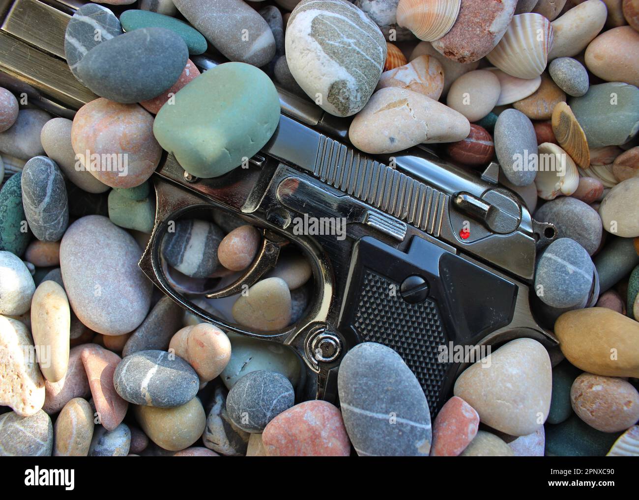 Scartato pistola automatica mezzo sepolto in pietre di mare Foto Stock