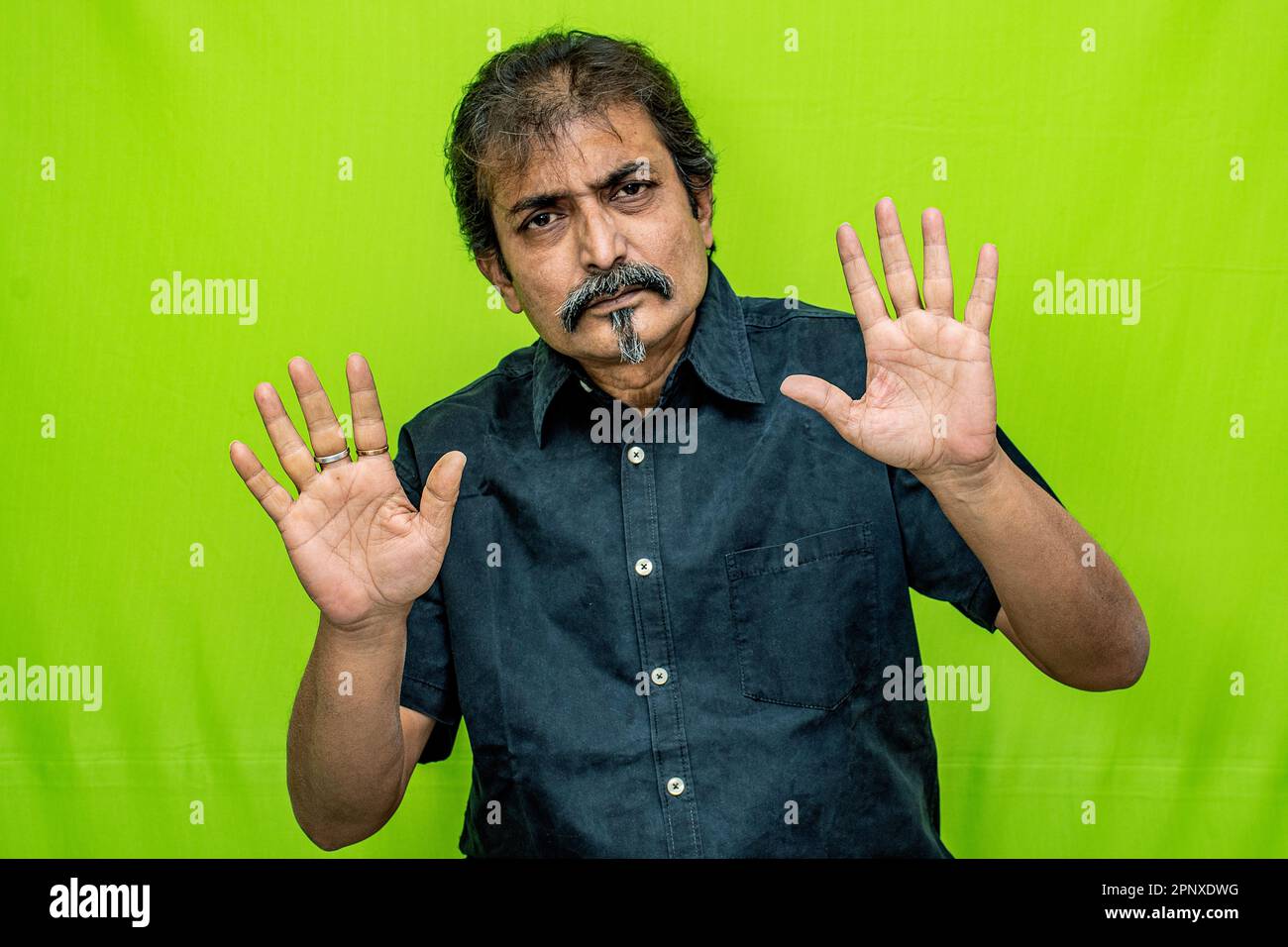Un uomo d'affari in camicia nera, in piedi contro uno schermo verde, segnali stop a quelli di fronte con entrambe le mani e gesti con disgusto Foto Stock
