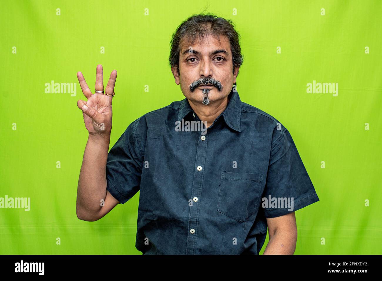 Un uomo d'affari intelligente in camicia nera mostra "quattro" con le dita della mano destra, in piedi su uno sfondo verde Foto Stock