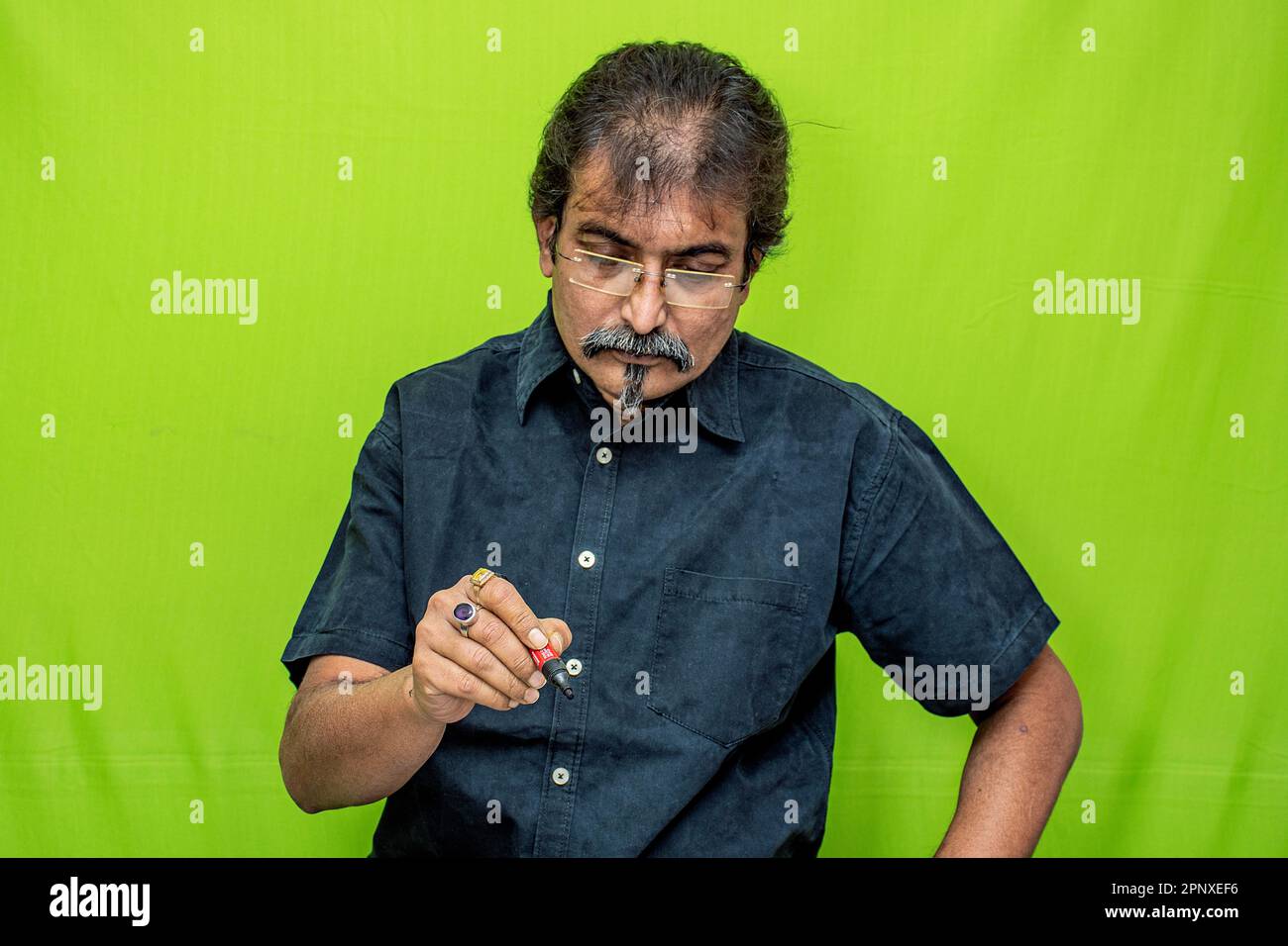 Un gentleman corporativo, in una camicia nera e occhiali, è seduto su uno sfondo verde schermo, e scrivere qualcosa con una penna sul tavolo di studio Foto Stock